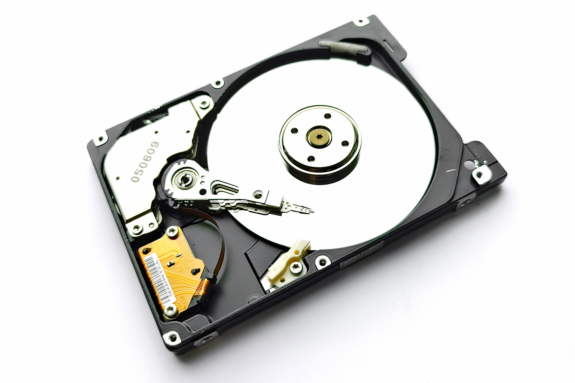 An opened 2.5-inch laptop hard drive with a shiny round platter, an arm with a head and a gold flexible cable