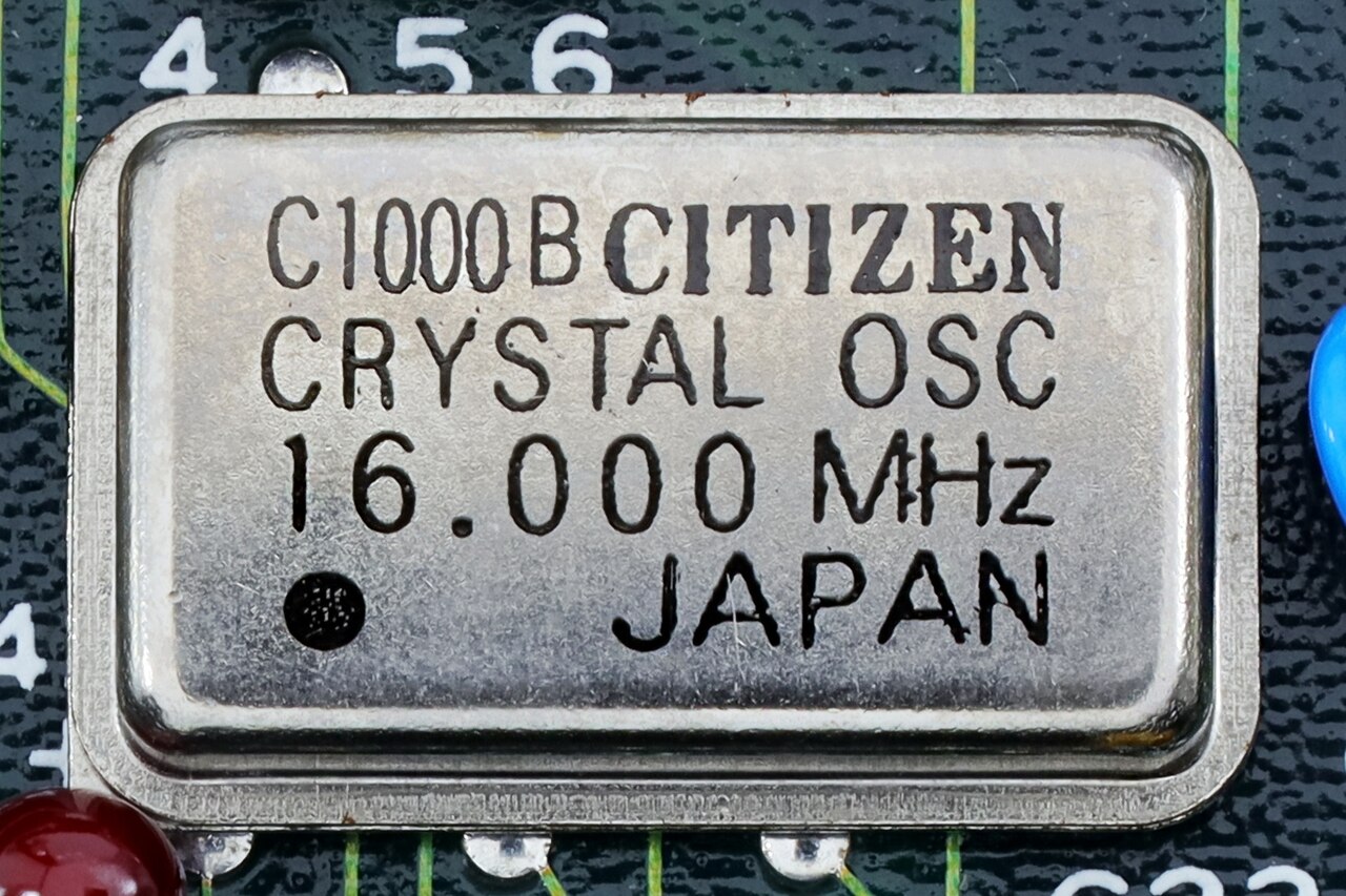 A small silver metal can crystal oscillator marked 16.000 MHz