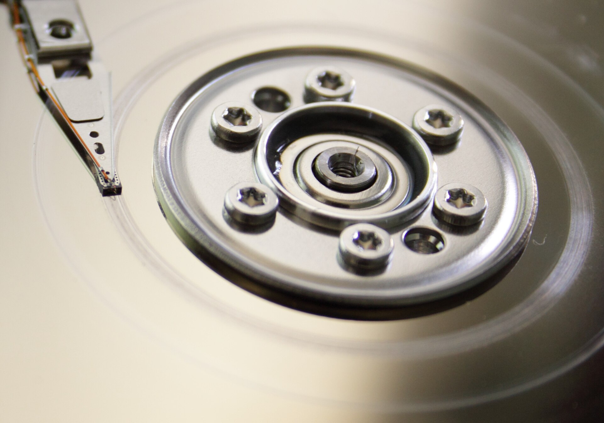 Close-up of a hard drive platter showing the central hub with six star-shaped screws and the tip of the actuator arm with the read/write head