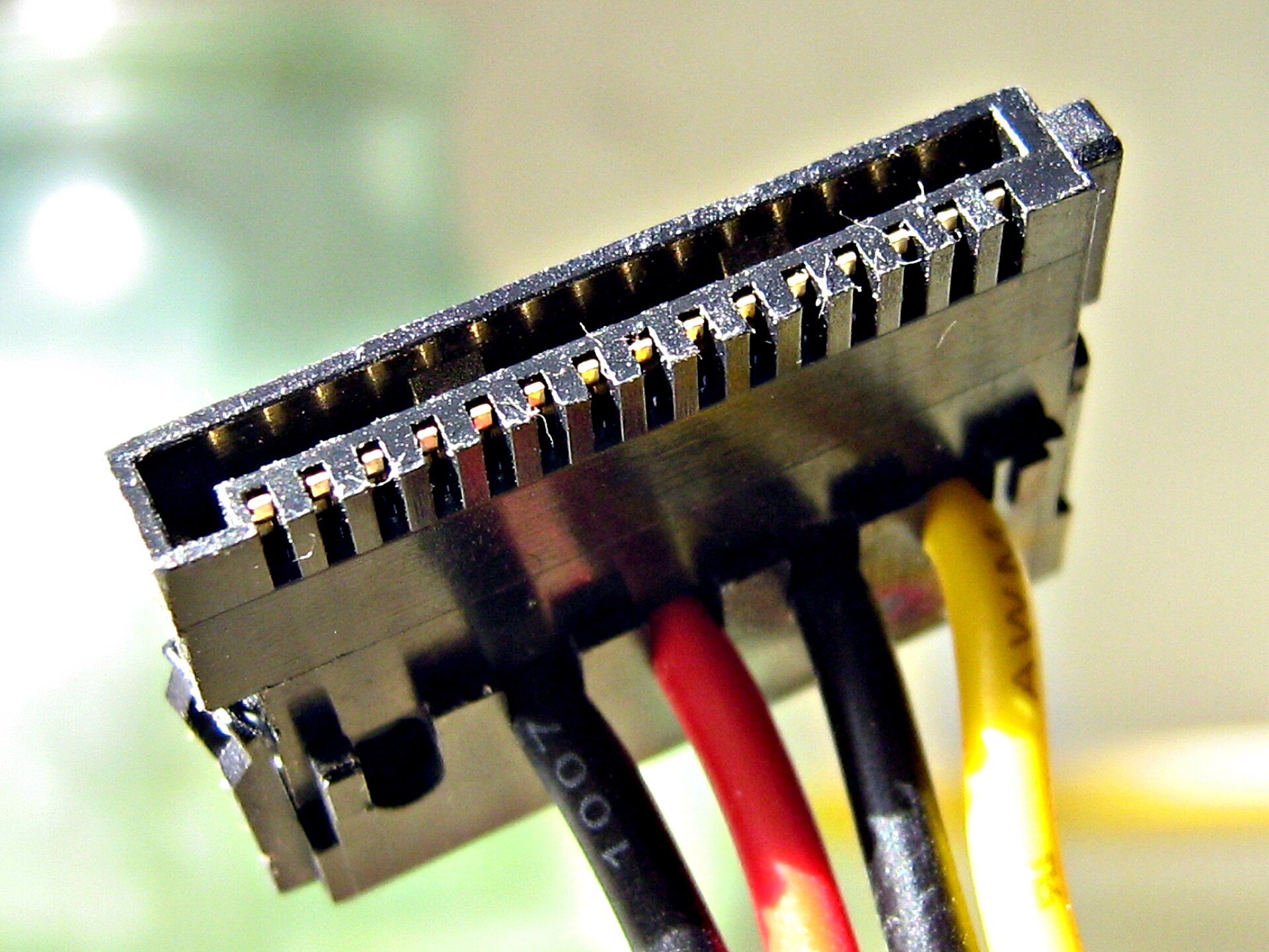 Extreme close-up of a SATA power connector showing a flat black L-shaped plastic housing with gold contacts and black, red, black and yellow wires