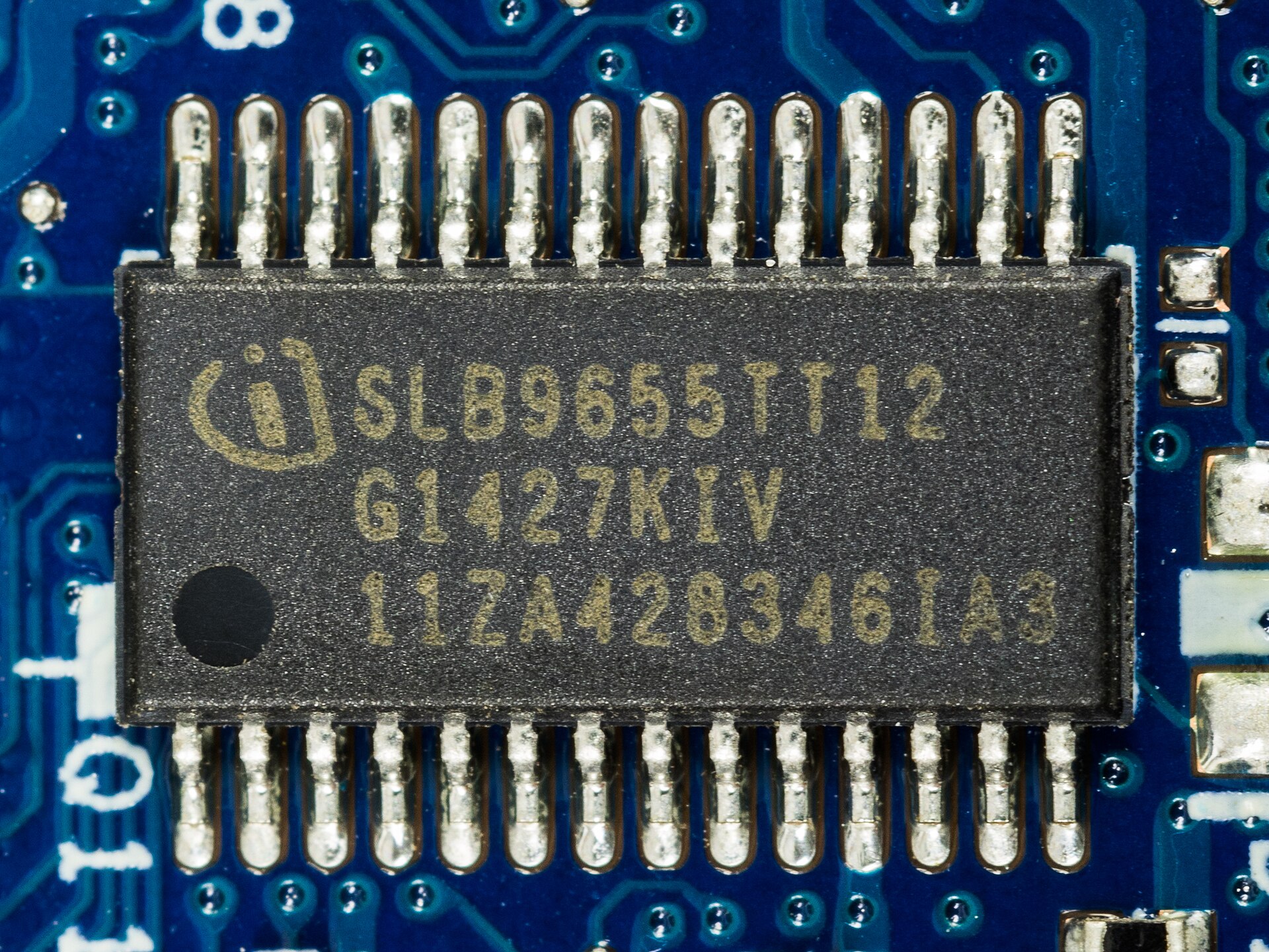 Close-up of a black TPM chip with 28 legs soldered on a dark blue circuit board, printed with the Infineon logo