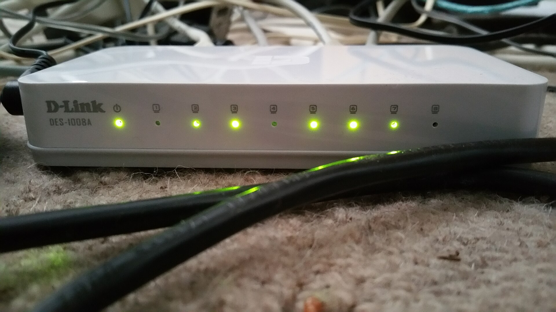 The front of a small white 8-port Ethernet switch with a row of small lights numbered 1 to 8 and a power light