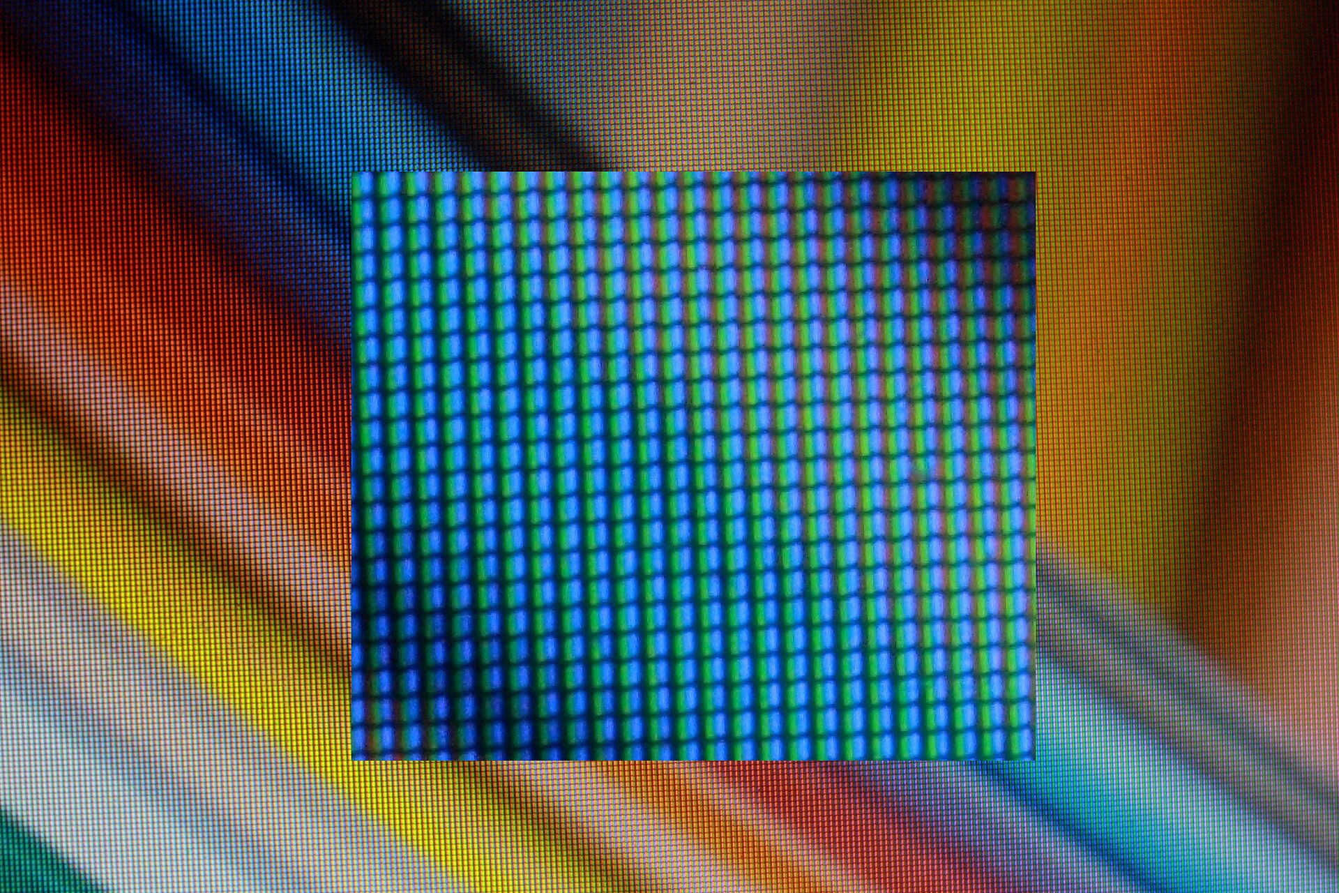 Extreme close-up of an LCD screen showing a regular grid of tiny coloured stripes, with a magnified blue-looking inset in the middle