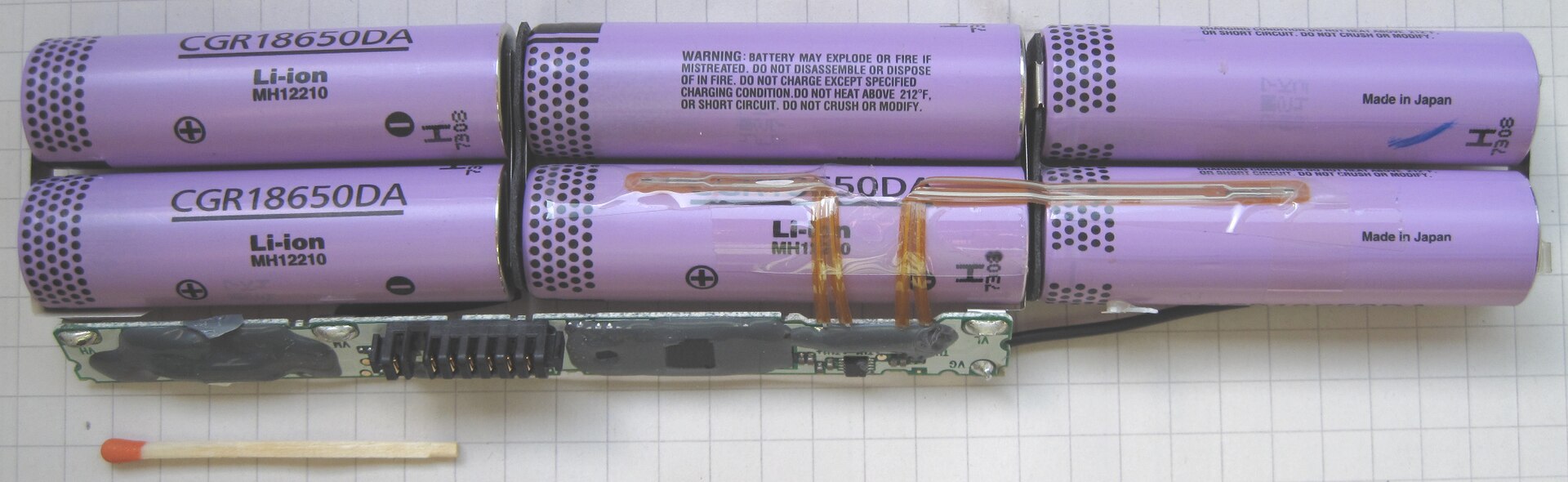 Inside a laptop battery pack: six purple cylindrical cells in two rows of three, with a thin circuit board and orange strips